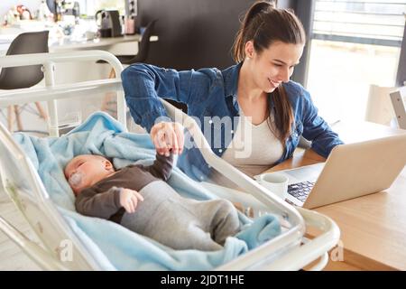 Sorridente madre che lavora sul pc e tiene la mano del bambino accanto ad esso in ufficio domestico Foto Stock