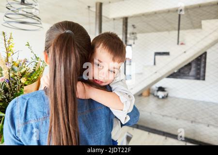 Il ragazzino abbraccia la madre per il suo compleanno e le dà un bouquet di fiori Foto Stock