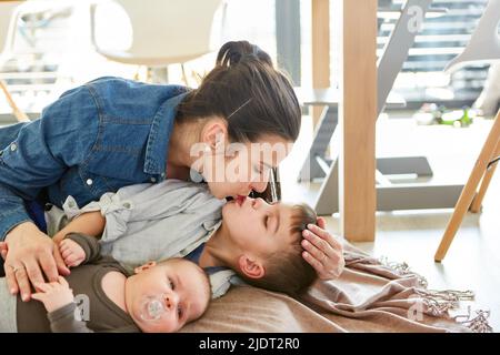 Mamma felice coccola con due figli e dà un bacio amorevole al fratello maggiore Foto Stock