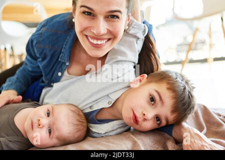 La mamma felice coccola con il bambino e il bambino come grande fratello a casa nel soggiorno Foto Stock