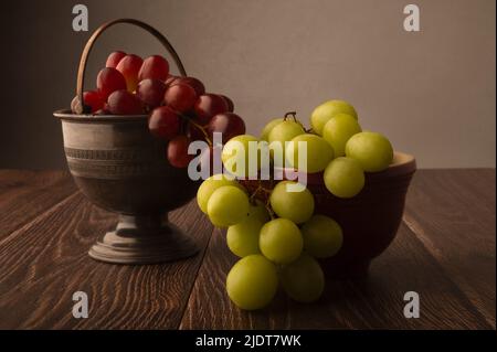 uve rosse e verdi in ciotole su tavola di legno scuro, con sfondo grigio, con spazio di copia sopra. Foto Stock