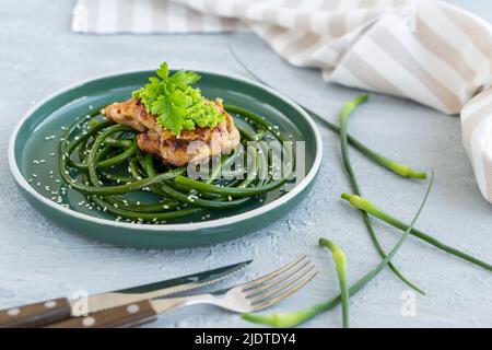 Bistecca di pollo fritta con frecce all'aglio e semi di sesamo in piatto verde su tavola grigia in cemento Foto Stock