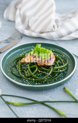 Bistecca di pollo fritta con frecce all'aglio e semi di sesamo in piatto verde su tavola grigia in cemento Foto Stock