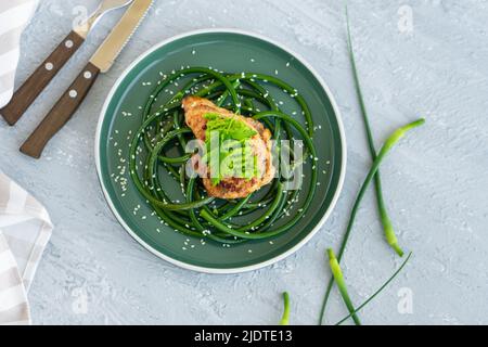 Bistecca di pollo fritta con frecce all'aglio e semi di sesamo in piatto verde su tavola grigia in cemento Foto Stock