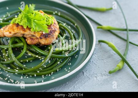 Bistecca di pollo fritta con frecce all'aglio e semi di sesamo in piatto verde su tavola grigia in cemento Foto Stock