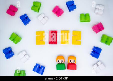 Blocchi di costruzione colorati, giocattoli figure in plastica: Ragazza in 2022 numeri e ragazzo verde su sfondo bianco. Foto Stock