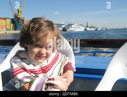 Crociera sul fiume. Una ragazza carina in un poncho a righe siede a bordo della nave e sorride. La barca naviga su un ampio fiume. Il concetto di viaggiare Foto Stock