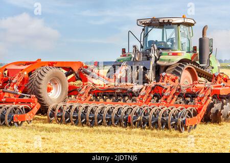 Un erpice a disco rosso si aggrappa ad un trattore agricolo gommato per coltivare la terra nei campi. Spazio di copia. Foto Stock