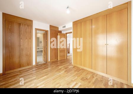 Camera da letto vuota con finestre in alluminio bianco, pavimento in parquet di quercia e armadi abbinati a muro su diverse pareti Foto Stock