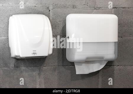 Dispenser di carta asciugamani e asciugatrice a mano su pareti di cemento su un bagno moderno ed elegante in stile loft Foto Stock