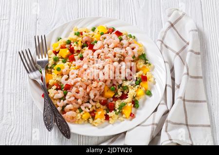 gamberi per insalata cotti conditi con porridge di miglio con piselli verdi, mango, peperoni rossi su piatto bianco su tavola di legno bianco Foto Stock