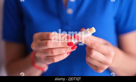 Donna con manicure rosso che tiene il rossetto igienico nelle mani primo piano Foto Stock