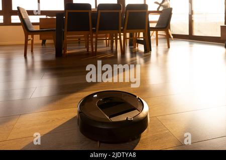 Aspirapolvere robotizzato su pavimento in legno laminato in sala da pranzo sotto la luce del sole Foto Stock