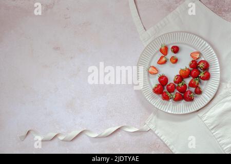 Ricette per la cottura estiva. Fragole in un piatto su un grembiule mockup. Testo sfondo, dolci dolci. Vista dall'alto. Foto Stock