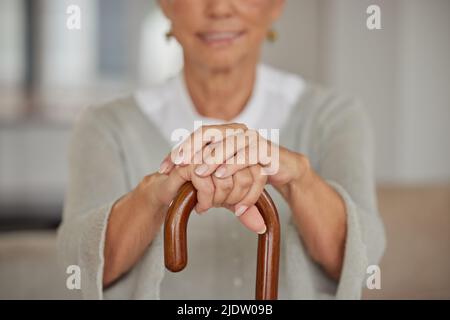 Donna anziana disabile che tiene una canna all'interno di una casa di cura. Primo piano di una donna anziana in possesso di un aiuto per camminare, rilassarsi in una struttura sanitaria mentre Foto Stock