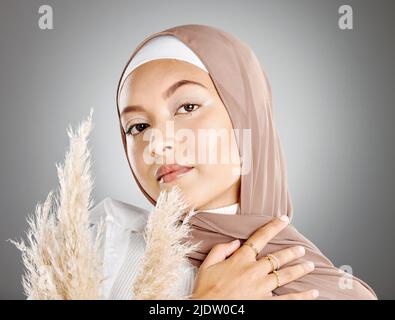 Studio ritratto di una bella giovane donna musulmana con foulard marrone posa con pampas pianta di grano su sfondo grigio. Arabo modesto Foto Stock