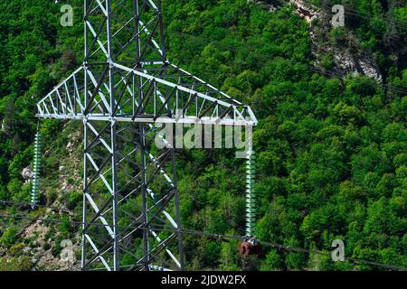 frammento di un palo di trasmissione di potenza in primo piano sullo sfondo di un pendio boscoso di montagna Foto Stock