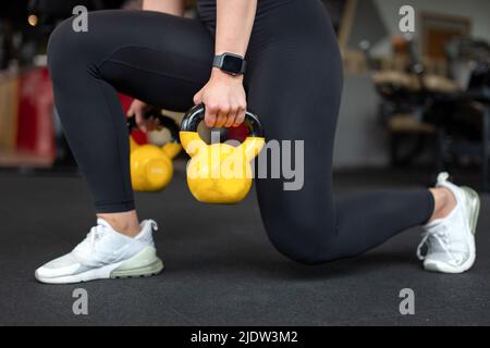 Donna che fa pranzi in palestra da due Kettlebell giallo closeup Foto Stock