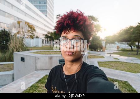 primo piano ritratto, giovane donna colombiana latina con afro e occhiali, grave infastidito prendere un selfie, vista frontale e telefono prospettiva Foto Stock