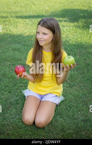 Una ragazza adolescente tiene le mele nelle sue mani mentre si siede sull'erba verde nel parco. Foto Stock