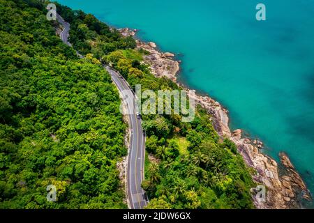Vista aerea della strada tra palme da cocco e il grande oceano di giorno a Nakhon si Thammarat, Thailandia Foto Stock