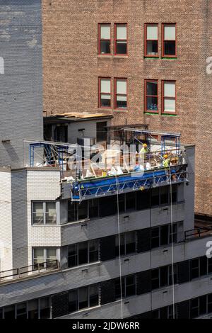 Lavoratori edili in alto sopra una strada urbana a New York City in un paniere sospeso, Midtown Manhattan, USA 2022 Foto Stock