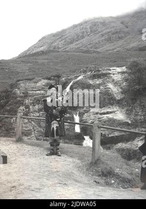 1950s, storico, un piper scozzese in kilt in piedi giocando le sue cornamuse, Highlands, Scozia, Regno Unito. Foto Stock