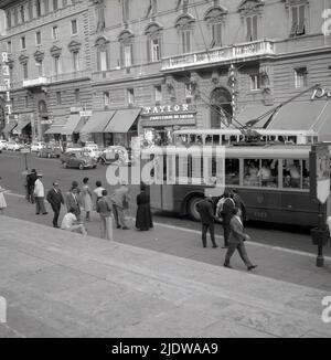 1950s, storico, Street scene, centro città, Napoli, Italia, con persone in attesa di autobus, il tram 75 in arrivo e un poliziotto in giacca bianca e cappello. Sul marciapiede sulla sinistra, si può vedere un piccolo cartello alla fermata dell'autobus che dice 'ferma Sussidiaria' (fermata temporanea). Foto Stock