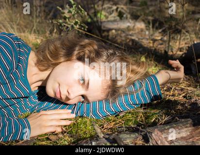 bella ragazza adolescente sdraiata sul muschio verde nella foresta godendo la luce del sole. relax all'aperto, la forza vitale della terra. ciao primavera, su Foto Stock