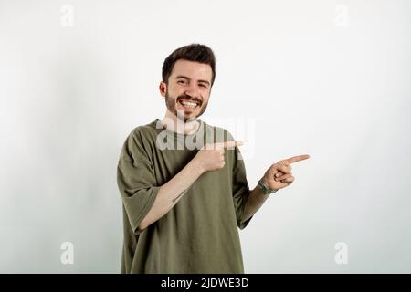 Giovane uomo allegro che indossa una t-shirt in posa isolata su sfondo bianco sorridendo e guardando la fotocamera puntando con due mani e dita al Foto Stock