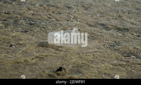 La coppa trasparente di plastica viene trasportata dal vento al mare nella zona costiera. Inquinamento plastico della zona surf. Mar Rosso, Egitto Foto Stock