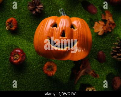 Allegra zucca sorridente arancione circondata da piccole zucche sull'erba verde. Sfondo - Halloween. Congratulazioni, invito, banner, pubblicità Foto Stock