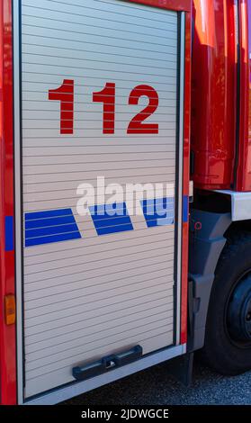 Sportello della serranda per camion antincendio su un motore antincendio tedesco con il numero di telefono di emergenza europeo 112 stampato Foto Stock