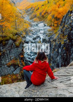 Autunno autunnale alberi e donna turistica si siedono sulla roccia vicino al canyon del fiume. Paesaggio di montagna con fiume Foto Stock