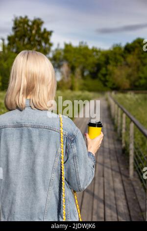 ragazza con la tazza di carta gialla che cammina nel parco. Foto di alta qualità Foto Stock