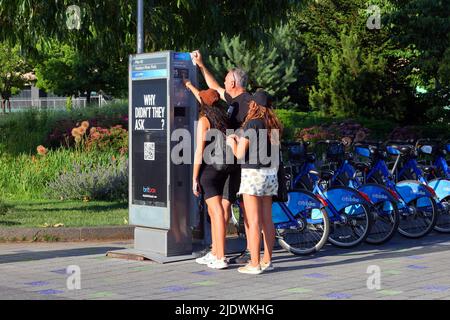 I turisti puntano alla segnaletica su un chiosco Citibyke a Hudson River Park, New York City. Condivisione biciclette, noleggio biciclette. Foto Stock