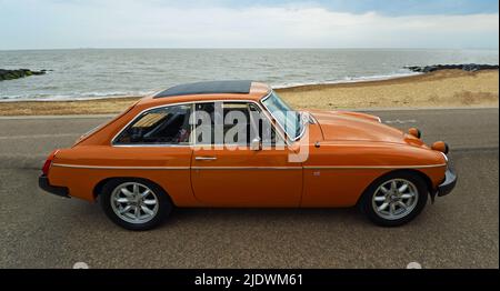 Classic Orange MGB GT parcheggiato sulla spiaggia lungomare e l'oceano sullo sfondo. Foto Stock