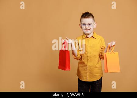 Shopping il Black friday. Ragazzino che tiene le borse dello shopping su sfondo giallo. Acquirente con molti sacchetti di carta colorati. Sconti e vendite vacanze. C Foto Stock