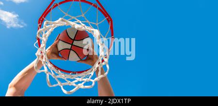 il giocatore di basket lancia la palla nel cerchio sullo sfondo del cielo, colpendo. Design poster orizzontale. Intestazione banner Web, spazio di copia. Foto Stock
