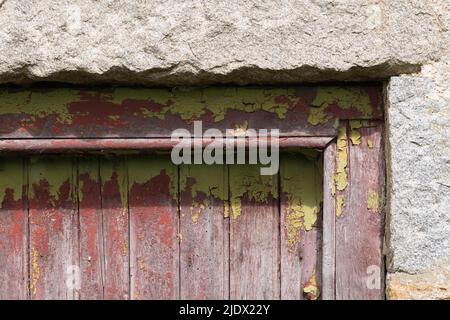 L'angolo superiore di una vecchia porta di legno giallo-verde, incorniciata da blocchi di granito, con vernice spaccata che mostra un colore di Crimson e Woodworm intemperie Foto Stock