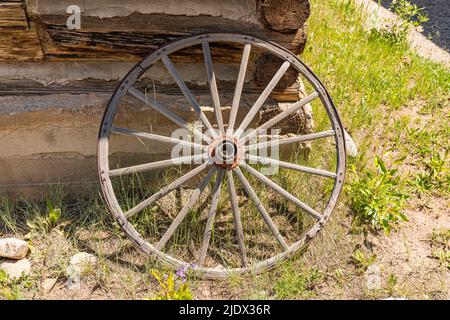 Vecchia ruota del carro resistente alle intemperie appoggiata contro una parete della cabina di legno Foto Stock
