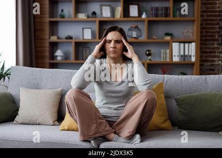Giovane donna turbata che soffre di mal di testa. Donna esausta con occhi chiusi massaggiando i templi con sensazioni dolorose. Emicrania, sangue alto Foto Stock