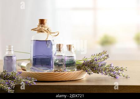 Contenitori di vetro con essenza di lavanda con mazzi di punte intorno su legno in una stanza. Vista frontale. Composizione orizzontale. Foto Stock