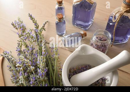 Preparazione fatta in casa di essenza di lavanda naturale con elementi per la preparazione e contenitori con liquido di lavanda in primo piano. Vista rialzata. Horizo Foto Stock