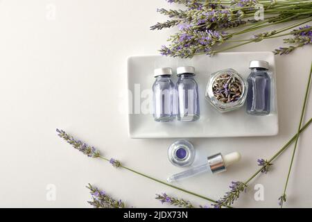 Estratto di lavanda medicinale in flaconcini su piastra su tavola bianca con un mazzetto di punte. Vista dall'alto. Composizione orizzontale. Foto Stock
