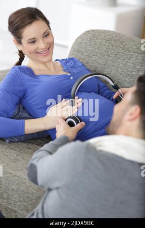 uomo che tiene le cuffie sul ventre della donna incinta Foto Stock