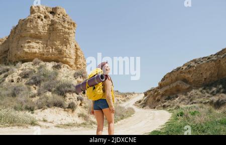 Donna sorridente che indossa zaino escursioni su strada sterrata Foto Stock