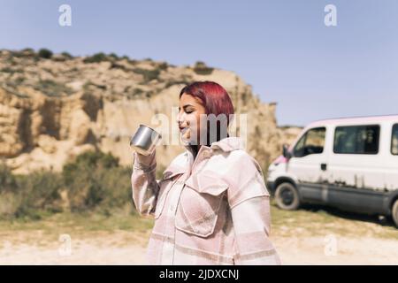 Donna sorridente con capelli rossi tinti che tengono la tazza in giorno di sole Foto Stock
