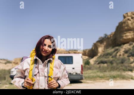 Donna sorridente con capelli rossi indossando zaino in giornata di sole Foto Stock