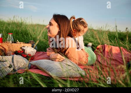 Giovane donna sorridente sdraiata di fronte alla figlia in campo agricolo Foto Stock